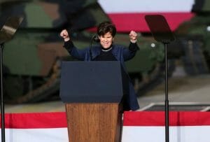 A woman stands at a lectern with both fists raised.