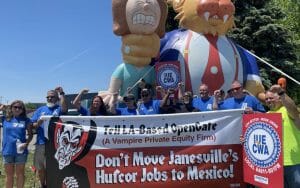 11 workers in Janesville, Wisconsin holding a banner that reads, "Don't Move Janesville's Hufcor Jobs to Mexico"