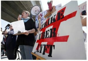 Person speaking into a bullhorn by a banner with the slogan "Strike Uber Lyft"