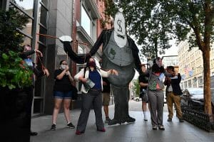 A cardboard cut out of a banker puppeteers two protesters dressed as members of Congress.