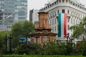 A pedestal in the middle of a street with a building and red, green, and white flag hanging in the background.