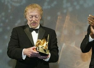 Man in a tuxedo holding a gold award statue.