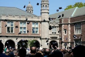 College students throw their caps in their air in front of a brick college building
