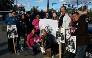 A group of people hold picket signs stating "GM stop your war on the working class."