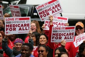 A group cheers and holds signs supporting Medicare for All outside.