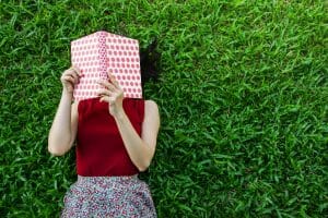 woman laying down on grass reading a book