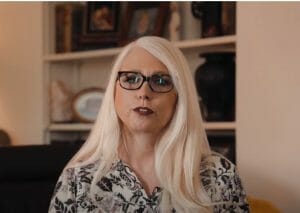 A woman with long white hair and black glasses.