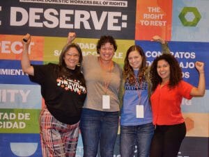 Four advocates for domestic workers pose with arms raised in celebration.