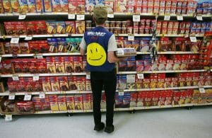 A worker is stocking shelves wearing a vest with the Walmart logo on it.