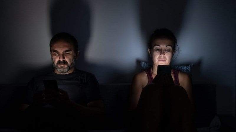 Two people in the dark illuminated by screens, not speaking to one another