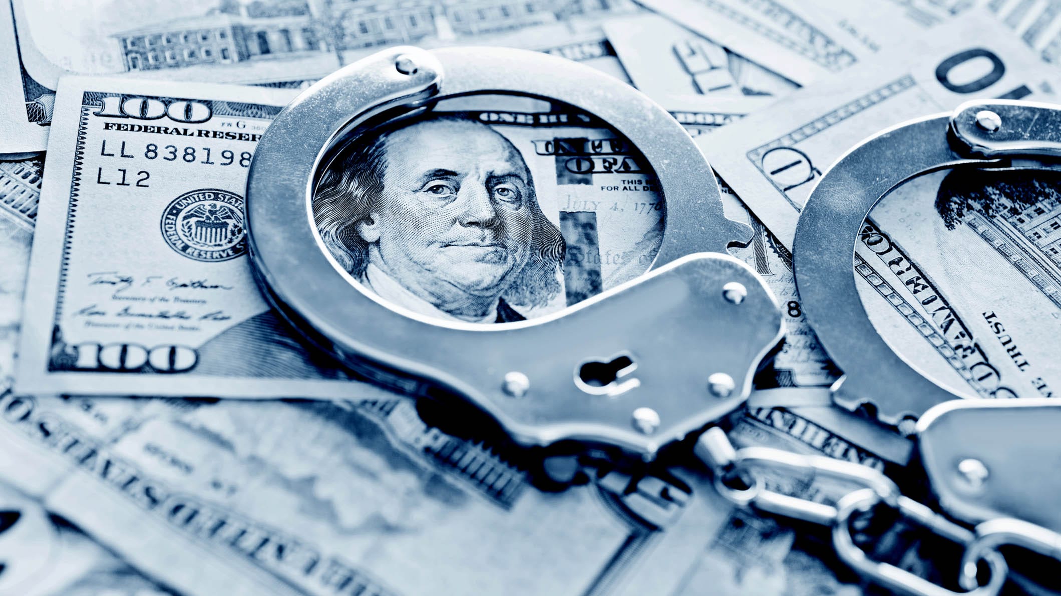 A picture of handcuffs framing Benjamin Franklin's portrait on a hundred dollar bill