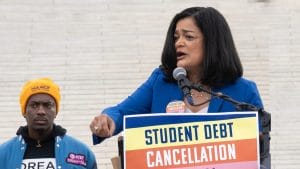 A woman stands at a podium with a sign saying "Student Debt Cancellation."