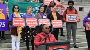 People are standing on steps holding signs saying "Not Tax Cut for the Super-Rich"