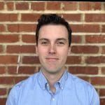 A man looks at the camera with a brick wall behind him.